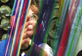 A person wearing ear protection stands behind brightly coloured threads.