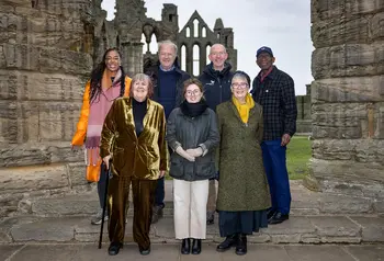 A group of seven men and women standing in front of the Whitby Abbey ruins