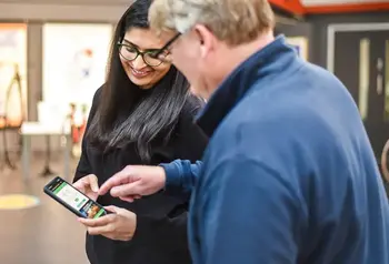 A woman holidaing a mobile phone, showing a man standing next to her something on th ephone screen.