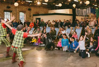 Two clowns performing in front of a crowd seated in deck chairs. Photograph by Graeme Oxby.