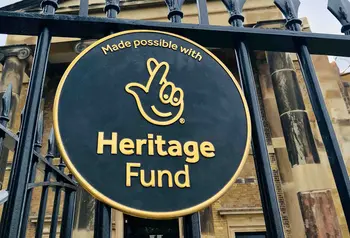 A round plaque of our acknowledgment stamp affixed to an iron fence. A building can be seen in the background.