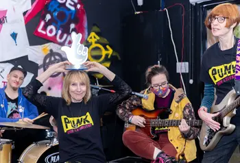 Four people play musical instruments including the drums and guitar in front of memorabilia from the Punk era