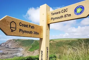 A wooden signpost pointing one way to Plymouth 300 miles away, and another way to the Tamara Coast to Coast route with Plymouth 87 miles away.