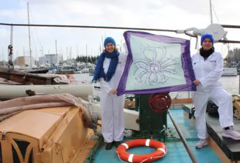 Photograph of two women holding up a flag while standing on a boat.