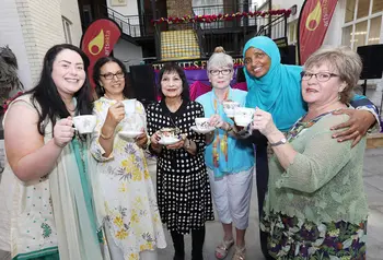 A group of six women standing side by side with raised tea cups in their hands