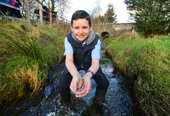 A boy holds a fish in the Ballinderry River