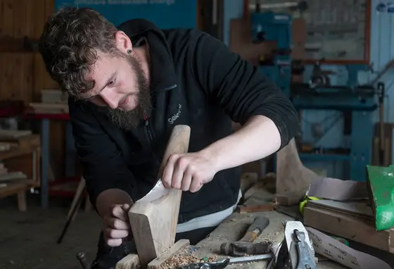 A man in a workshop sanding a piece of wood.