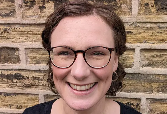 A close-up selfie of a woman with short hair standing against a brick wall