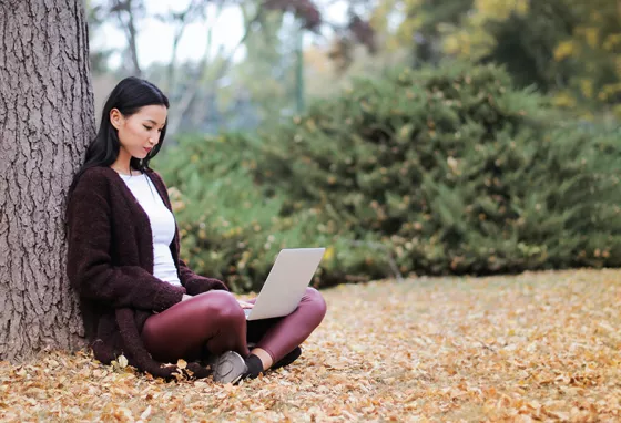 A young woman using a computer laptop under a tree