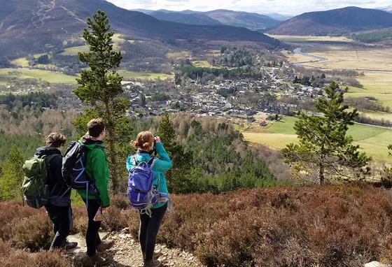 Three people look down over a valley with mountains in the distance