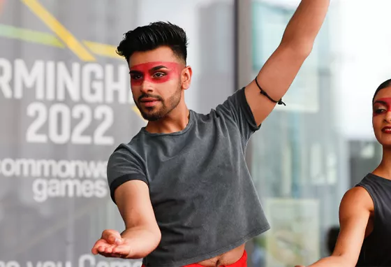 Two people striking a dance pose in front of a 'Commonwealth Games' sign 