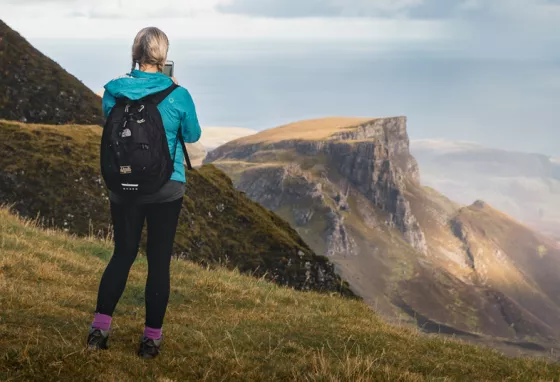 A person standing on a grassy mountainside, looking out to mountains in the distance