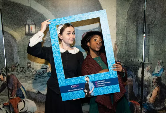 Image of two people in historic nursing outfits depicting Mary Seacole and Florence Nightingale, holding a frame to their faces