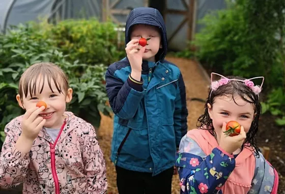 Three children hold tomatoes to their noses