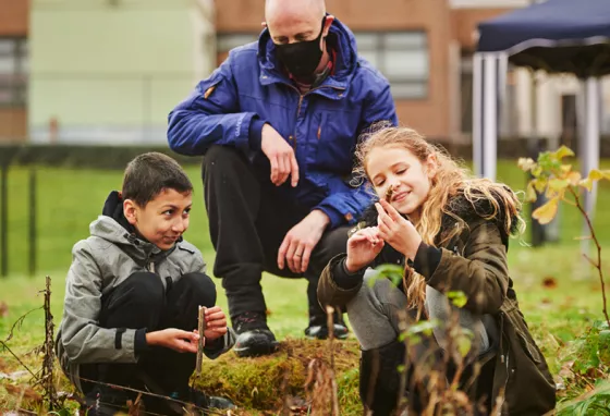 Two school children learning outdoors, watched over by a teacher