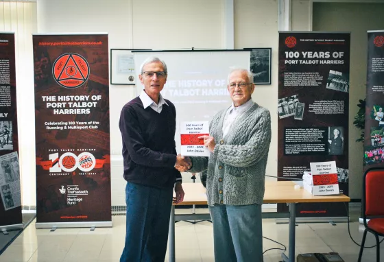 Two people standing in front of an exhibition for 100 years of the Port Talbot Harriers