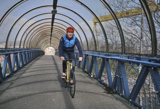 A man cycling on a bridge with the Harland and Wolff cranes visible in the background