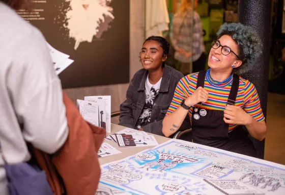 Young people talking at an event stall with posters and leaflets.