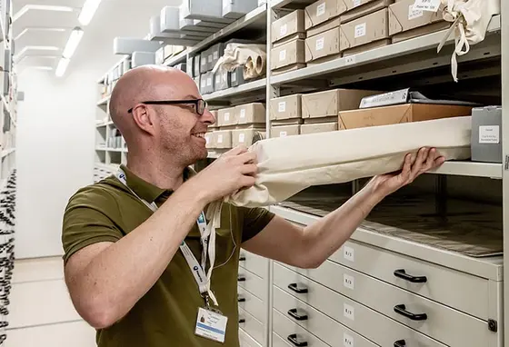 a man takes a cloth bag containing a rolled up document off a shelf in an archive