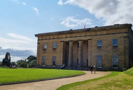 The facade of Belsay Hall on a sunny day, with visitors exploring the grounds