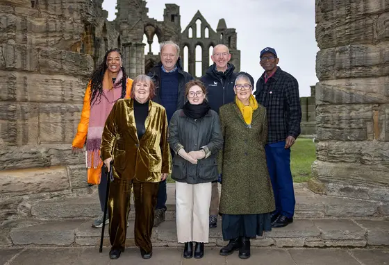 A group of seven men and women standing in front of the Whitby Abbey ruins