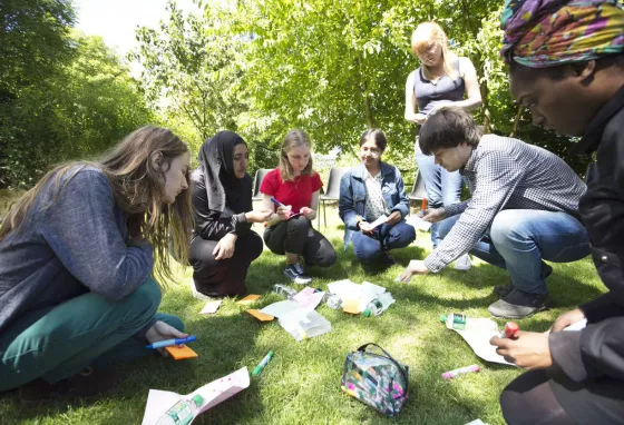 a group of young poeple in a circle on the grass, looking over papers and post-it notes