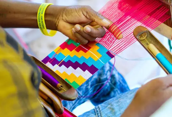 A close-up of a person's hands weaving colourful threads on a loom