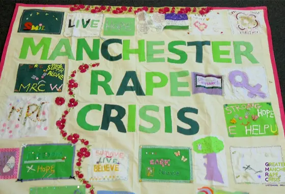 The banner has the words Manchester Rape Crisis in the middle with other phrases and images stitched around it