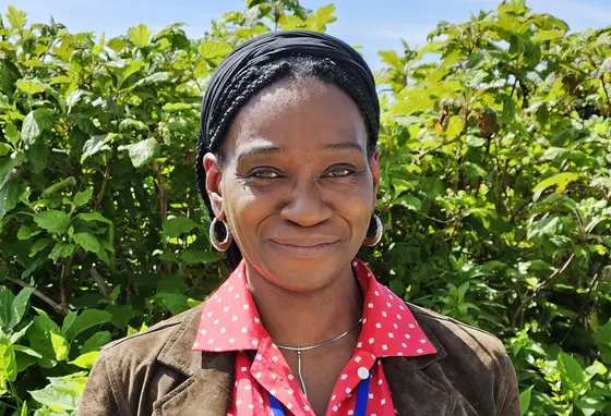 A head and shoulders portrait of a black woman standing in front of garden bushes