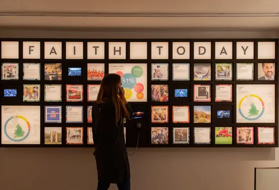 A visitor listens through an exhibition headset in front of a display of information about faith