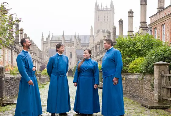 Members of Wells Cathedral’s Vicars’ Choral wear long blue robes and stand outside their medieval stone and brick homes on Vicars’ Close in Wells