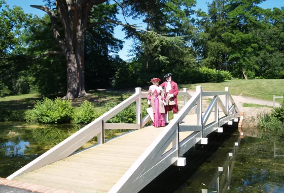 Two people in costume stand on a bridge in Painshill Park