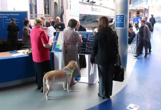 A visitor accompanied by a guide dog uses braille signage