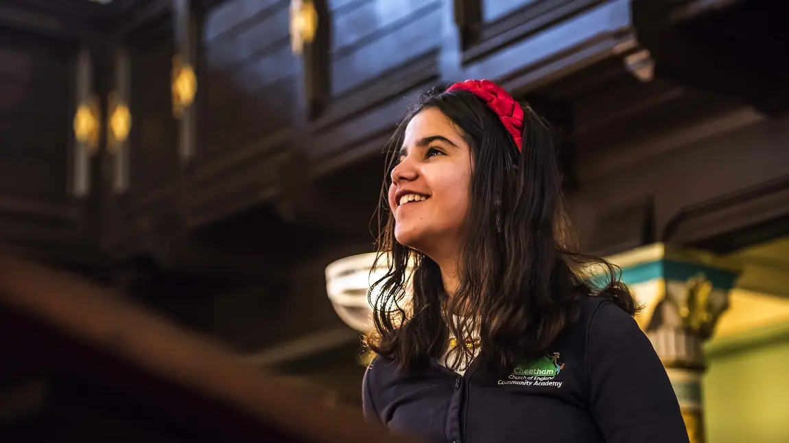 A young child in a school uniform looking up and smiling inside a synagogue