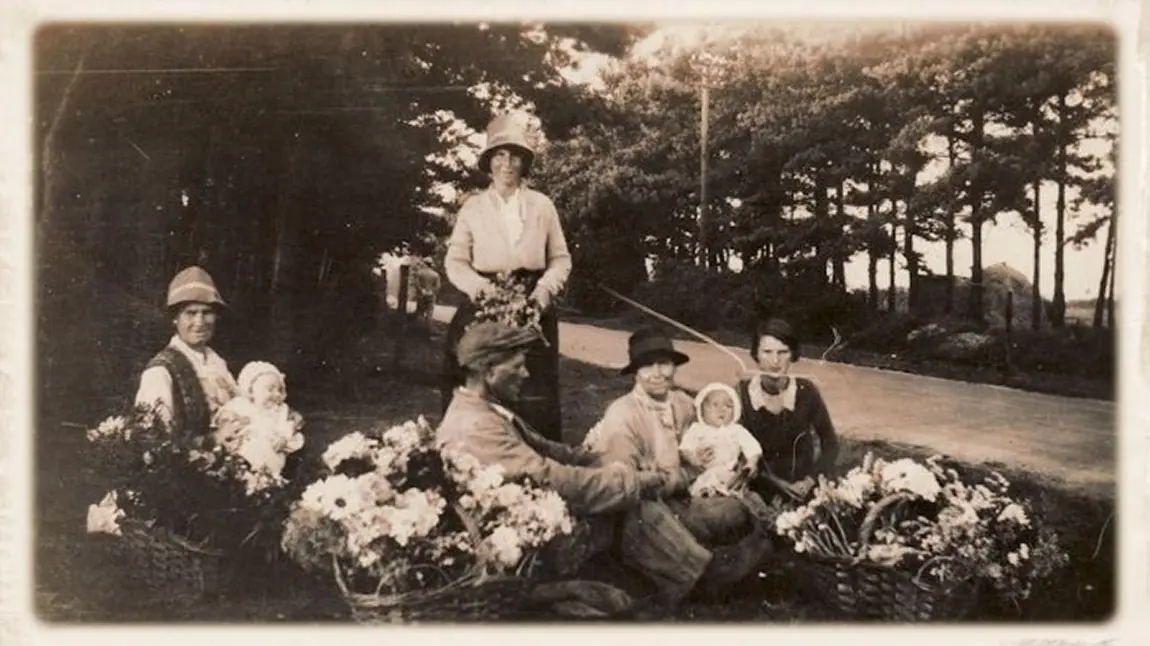A historic black and white photograph of a group of Traveller people with infants selling flowers