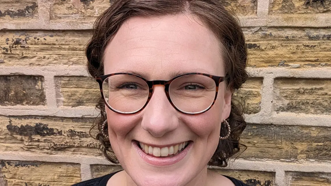 A close-up selfie of a woman with short hair standing against a brick wall