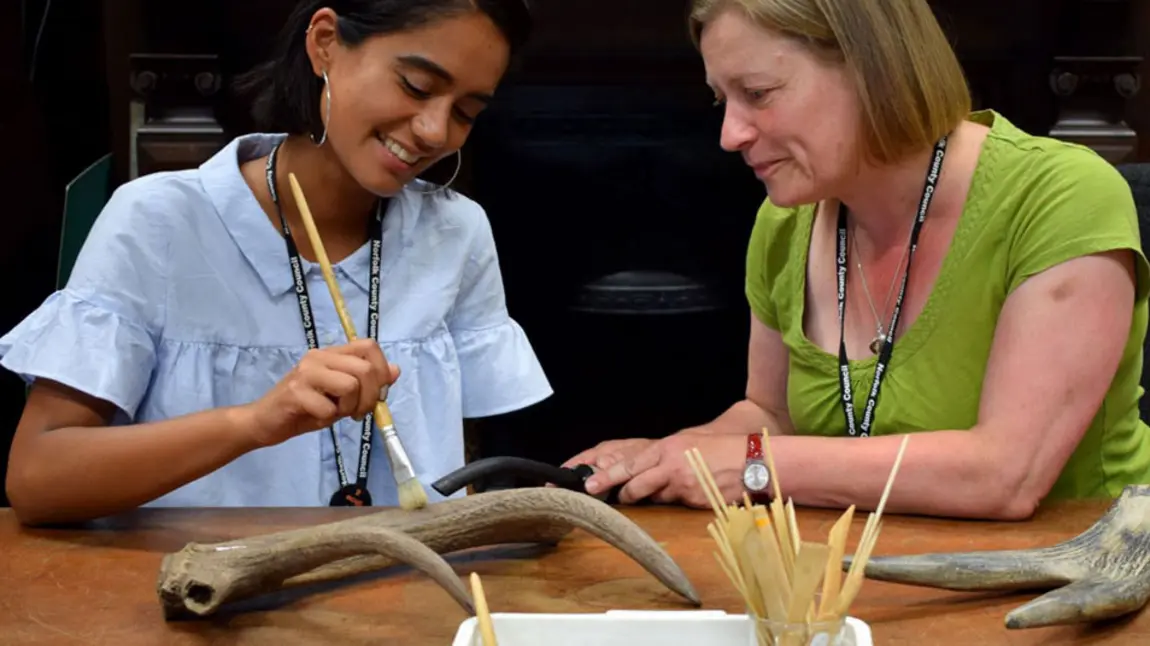 A woman watching as a younger woman cleans an antler behind the scenes at Norfolk Museums