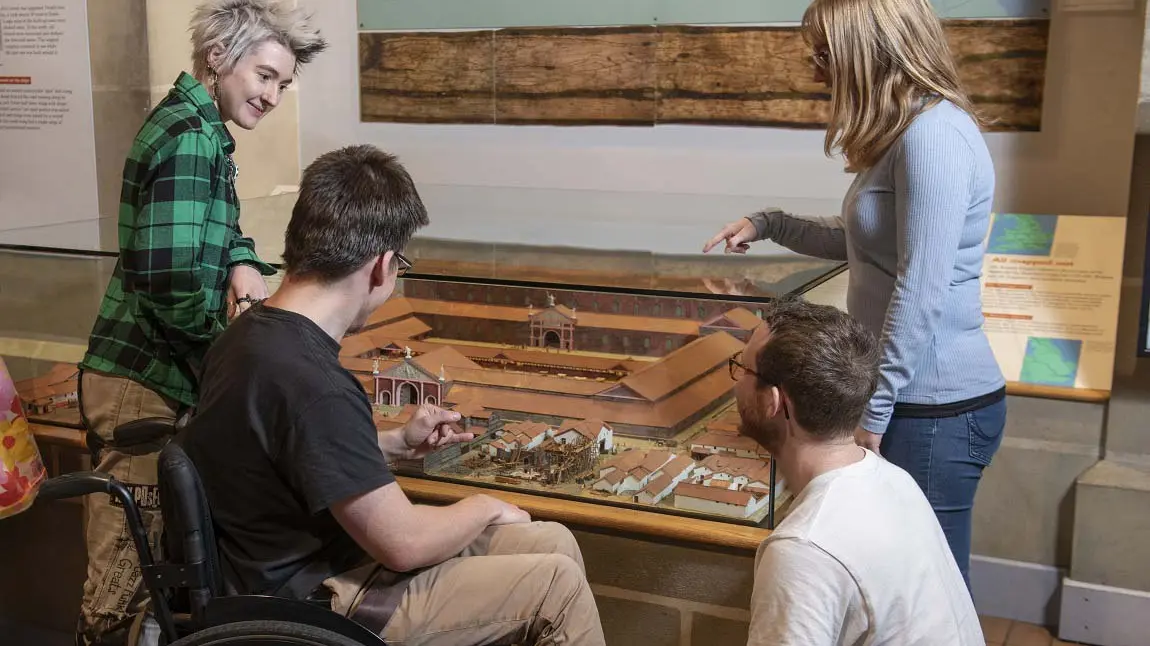 Four young people chatting and looking at a display of a small historical model settlement