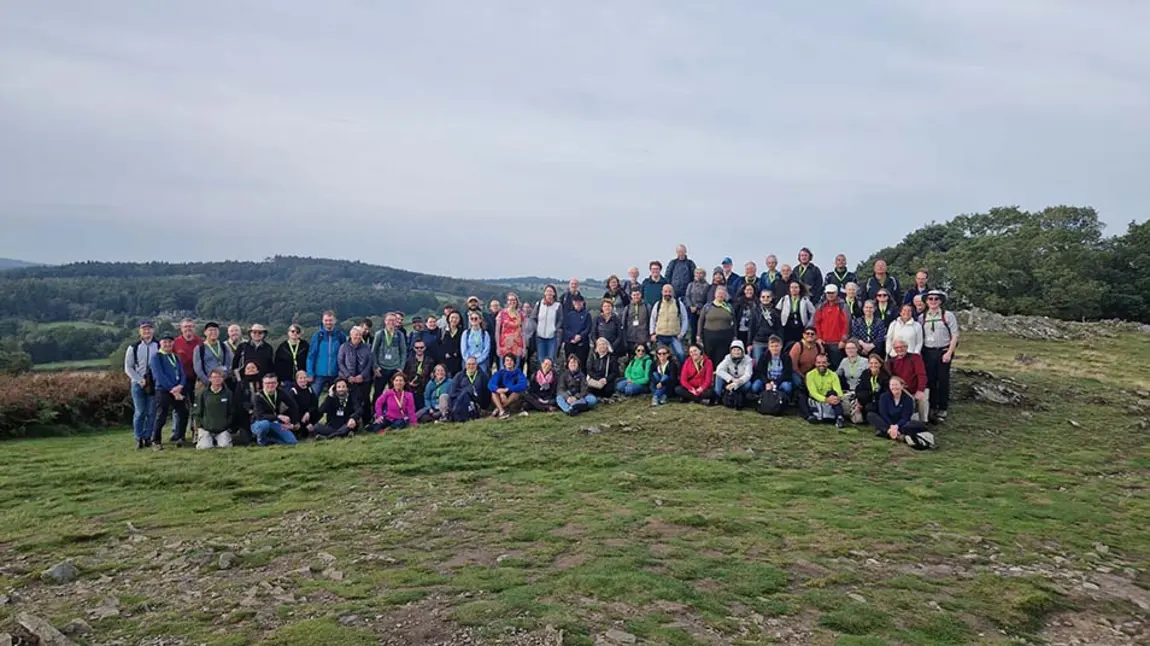 A large group of people wearing outdoor clothing pose for a group photo in the countryside