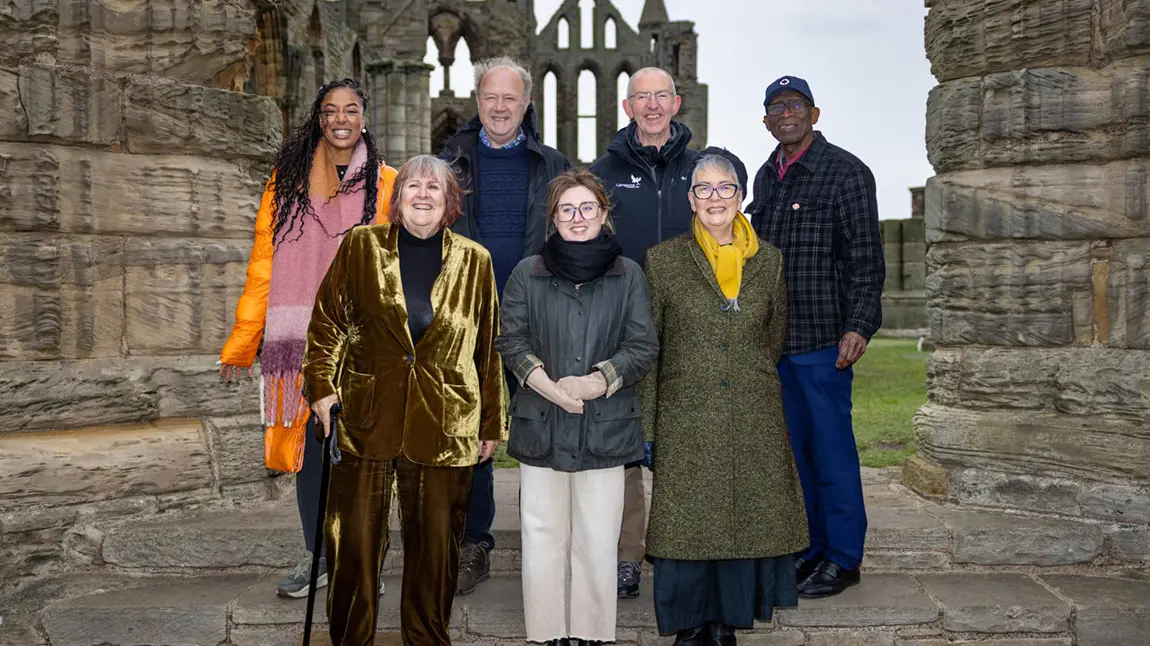 A group of seven men and women standing in front of the ruins of Whitby Abbey