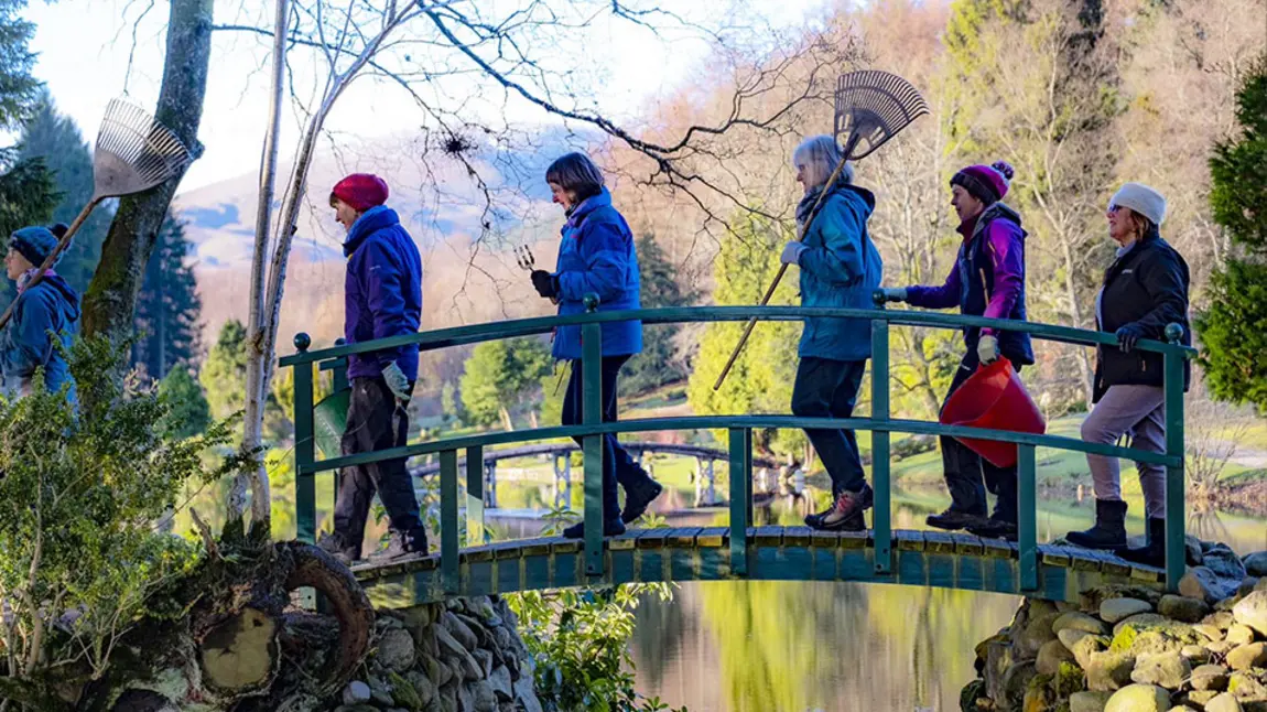 People walking across a bridge with gardening equipment in their hands