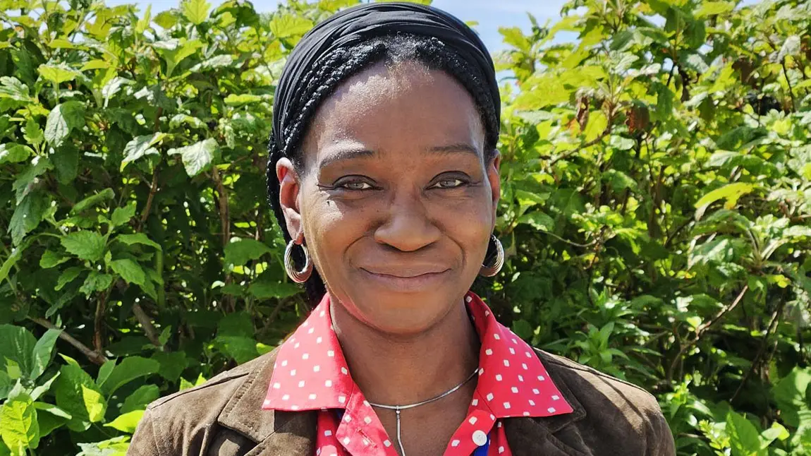 A head and shoulders portrait of a black woman standing in front of garden bushes