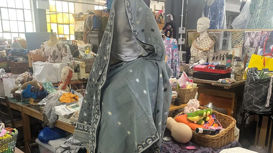 A mannequin with a Sari draped around is standing in a textile workspace