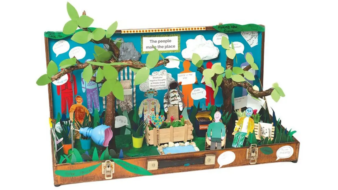 a memory box made during a craft activity at a mental health community centre: inside an old case is a garden scene with trees, planters and a pond, with figures and messages