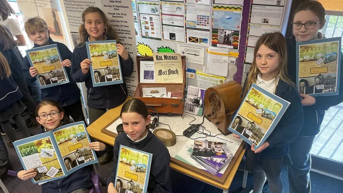 A group of school children hold books about life during the second world war and pose around a display related to the second world war 