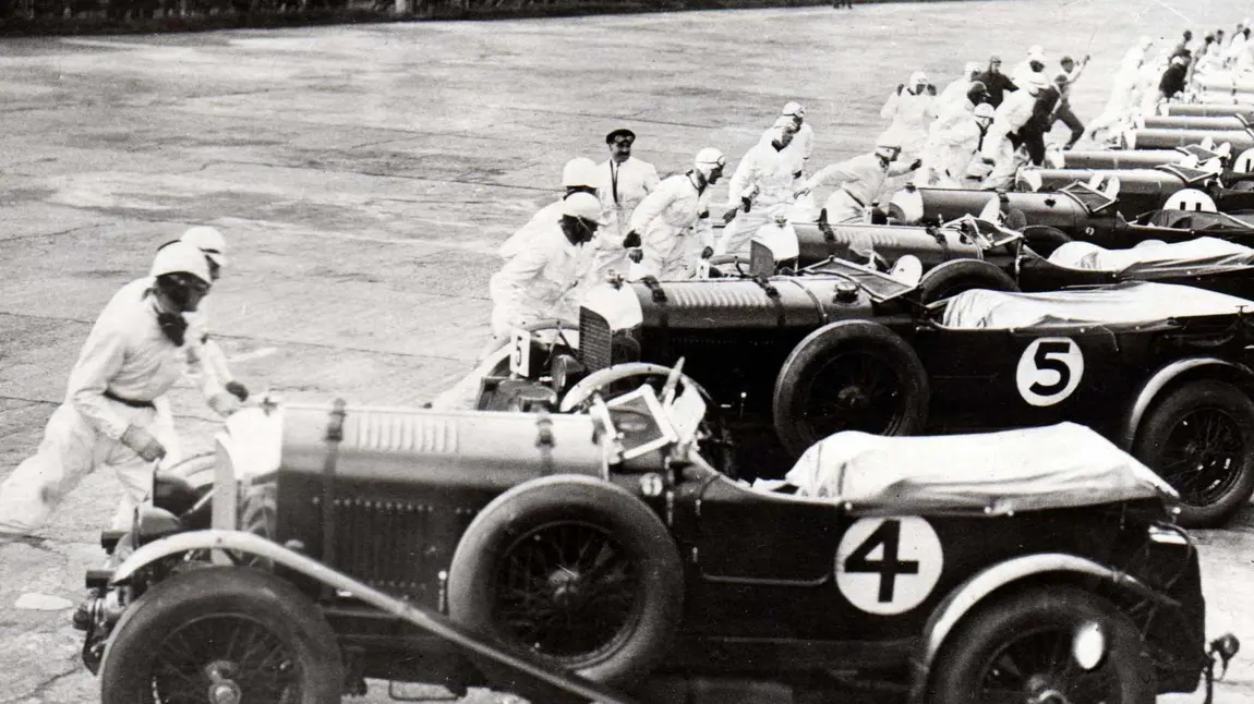 Cars ready to race at Brooklands in 1930 with the Vickers aircraft factory in the background