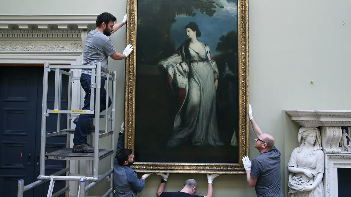 Workmen installing a painting by Sir Joshua Reynolds in the newly restored galleries