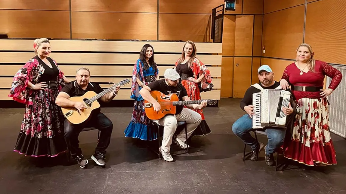 Three musicians with guitars and an accordion and four women dancers wearing traditional Eastern European dress.