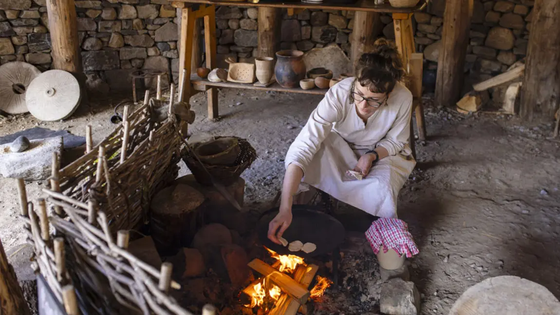 A person cooks on an open stove in a replica Iron Age roundhouse