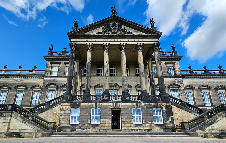 The facade of a stately home with a bright blue sky behind it